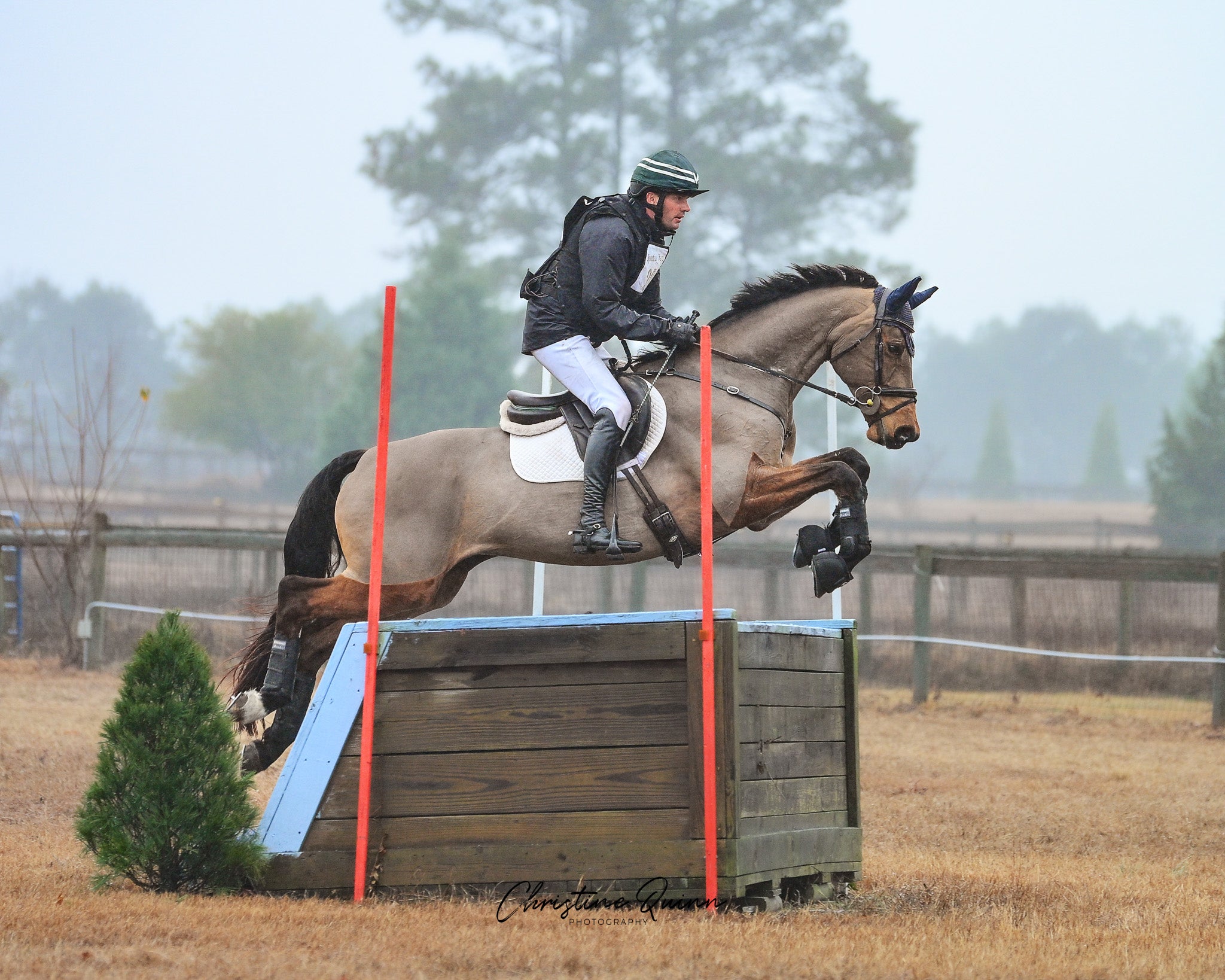 Horse and rider jumping over a box obstacle in foggy equestrian setting